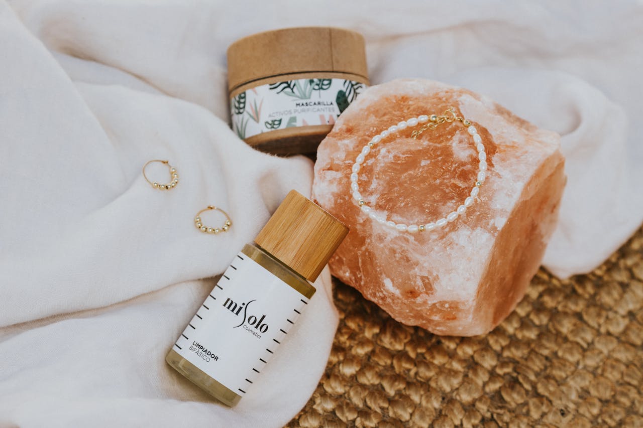 home-hero A flat lay of natural skincare products, a mineral stone, and jewelry on fabric.