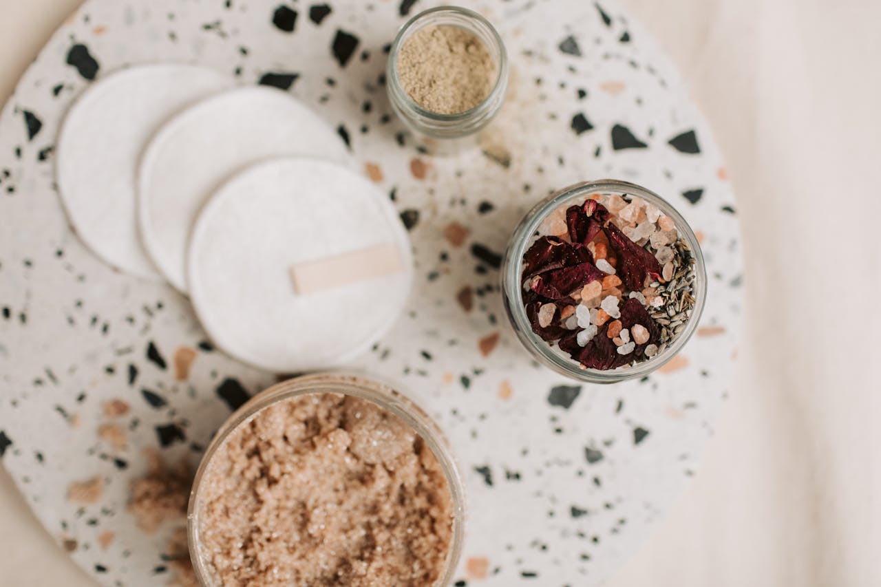 services-06 Flat lay of natural bath essentials including scrub and cotton pads on a terrazzo surface.