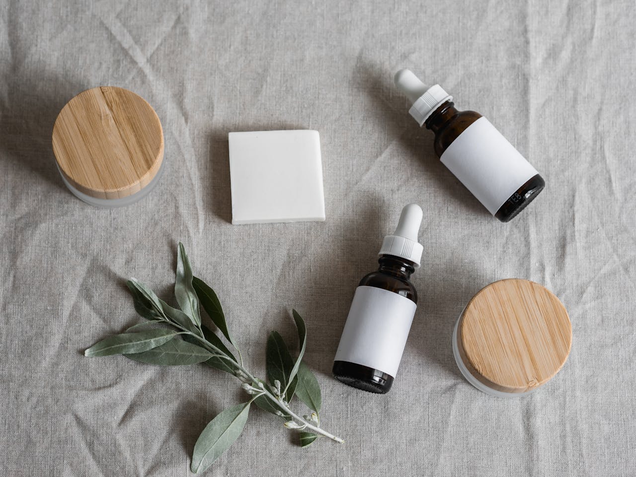 about-us Top view of skincare products with a natural theme, featuring bottles, jars, and a plant on linen cloth.